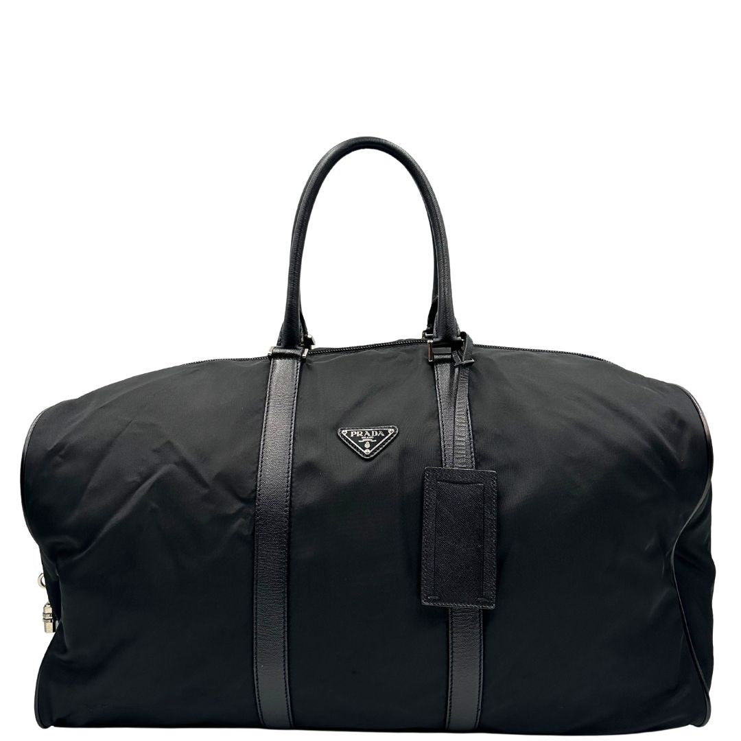 Front di un borsone Prada in nylon nero con finiture in pelle Saffiano tono su tono e parti metalliche argentate. Completo di dustbag, tag porta address e lucchetto. Indossabile a mano.