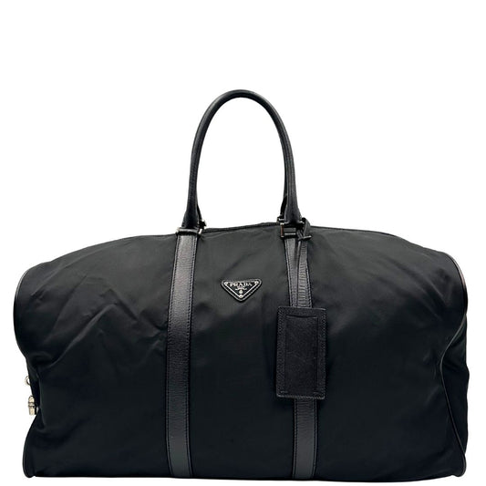 Front di un borsone Prada in nylon nero con finiture in pelle Saffiano tono su tono e parti metalliche argentate. Completo di dustbag, tag porta address e lucchetto. Indossabile a mano.