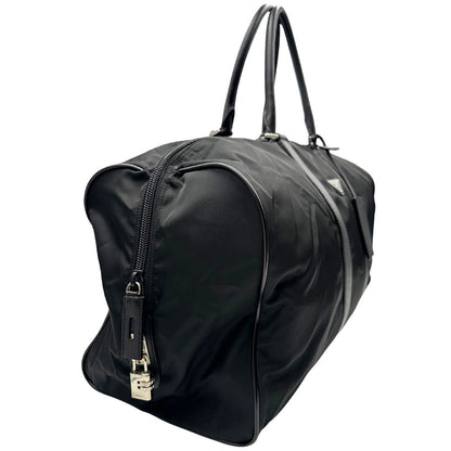 Laterale destro di un borsone Prada in nylon nero con finiture in pelle Saffiano tono su tono e parti metalliche argentate. Completo di dustbag, tag porta address e lucchetto. Indossabile a mano.