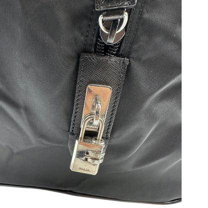Lucchetto di un borsone Prada in nylon nero con finiture in pelle Saffiano tono su tono e parti metalliche argentate. Completo di dustbag e tag porta address. Indossabile a mano.