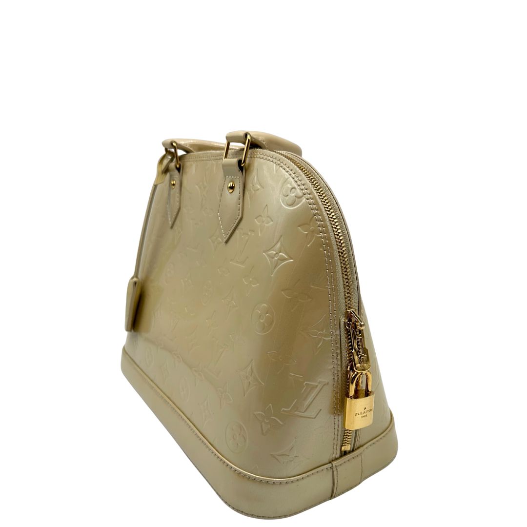 Laterale destro di una borsa Alma PM Louis Vuitton in pelle Vernis color noisette con parti metalliche dorate e doppi manici stondati; da portare a mano. Completa di lucchetto e chiavi. Indossabile a mano.