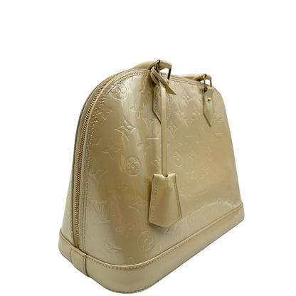 Laterale sinistro di una borsa Alma PM Louis Vuitton in pelle Vernis color noisette con parti metalliche dorate e doppi manici stondati; da portare a mano. Completa di lucchetto e chiavi. Indossabile a mano.