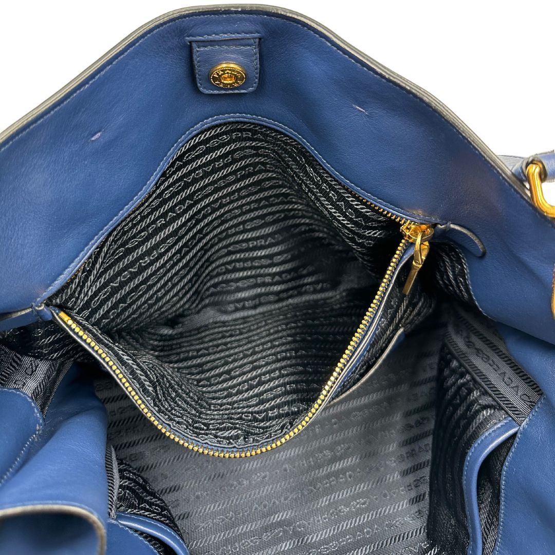 Interno di una borsa Prada in pelle bluette con parti metalliche dorate; munita di un accessorio porta address, doppi manici stondati e una tracolla amovibile e regolabile. Completa di dustbag e card d'autenticità. Indossabile a mano oppure a tracolla.
