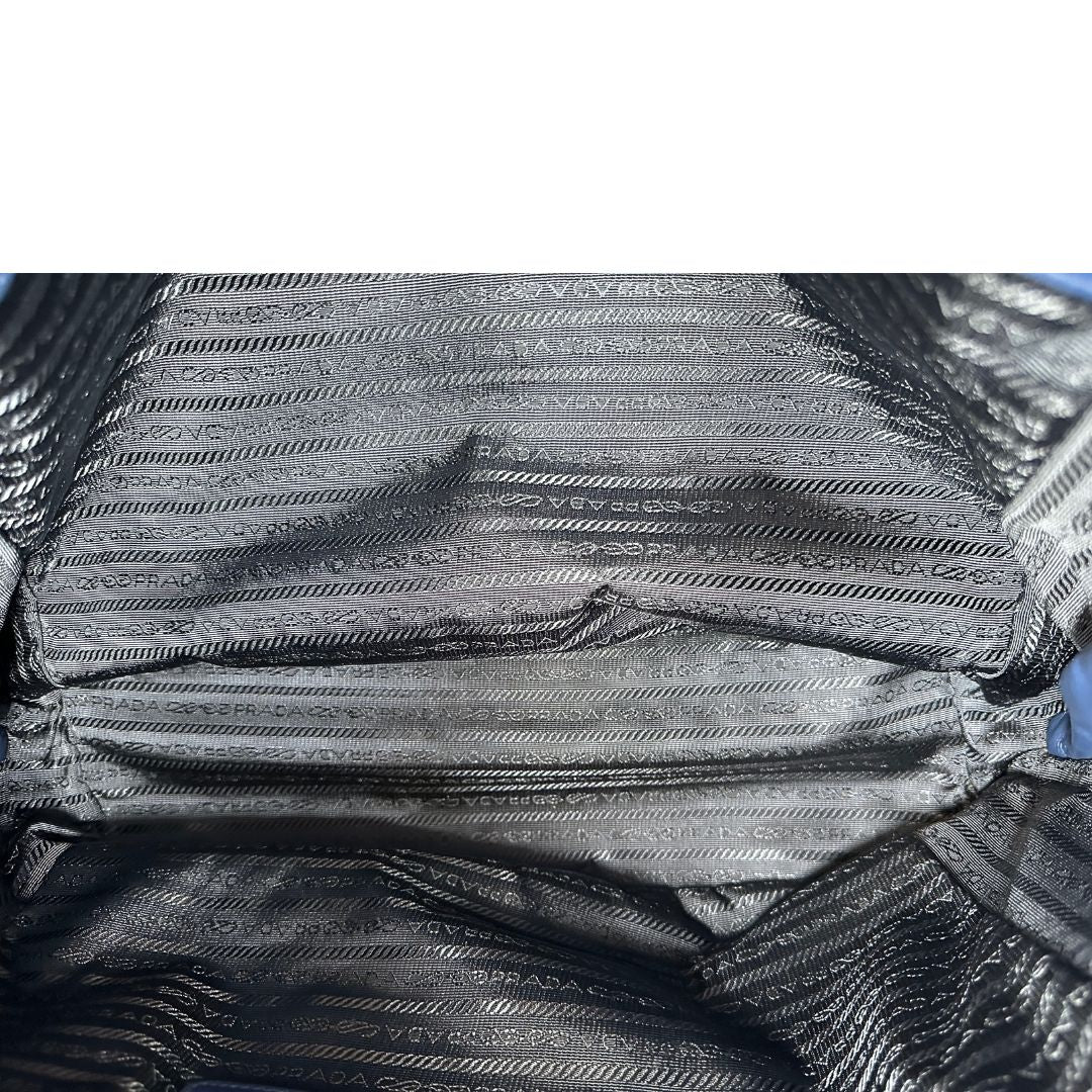 Interno di una borsa Prada in pelle bluette con parti metalliche dorate; munita di un accessorio porta address, doppi manici stondati e una tracolla amovibile e regolabile. Completa di dustbag e card d'autenticità. Indossabile a mano oppure a tracolla.