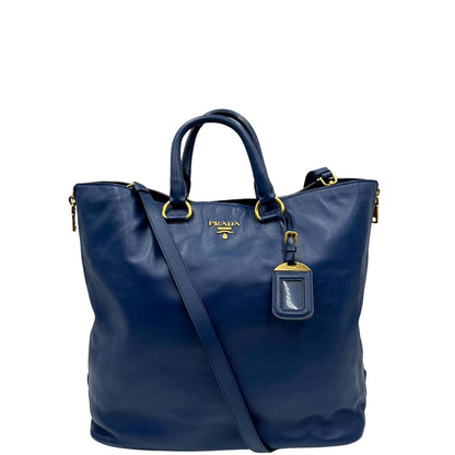 Front di una borsa Prada in pelle bluette con parti metalliche dorate; munita di un accessorio porta address, doppi manici stondati e una tracolla amovibile e regolabile. Completa di dustbag e card d'autenticità. Indossabile a mano oppure a tracolla.