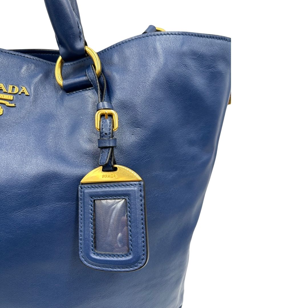 Tag porta address di una borsa Prada in pelle bluette con parti metalliche dorate; munita di doppi manici stondati e una tracolla amovibile e regolabile. Completa di dustbag e card d'autenticità. Indossabile a mano oppure a tracolla.