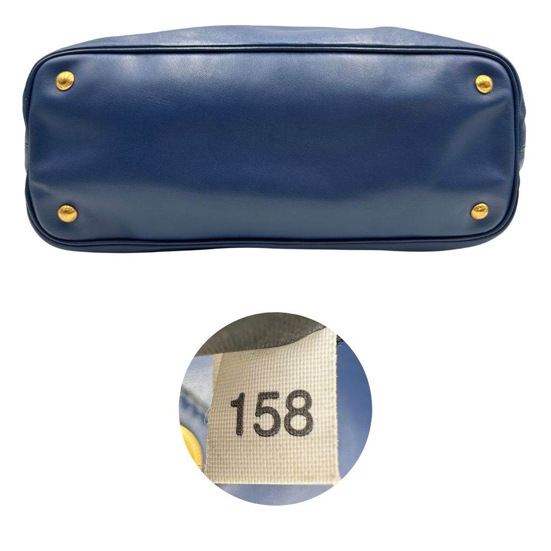 Base e codici di una borsa Prada in pelle bluette con parti metalliche dorate; munita di un accessorio porta address, doppi manici stondati e una tracolla amovibile e regolabile. Completa di dustbag e card d'autenticità. Indossabile a mano oppure a tracolla.