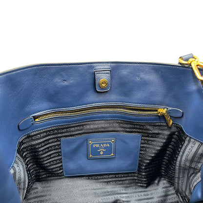 Interno di una borsa Prada in pelle bluette con parti metalliche dorate; munita di un accessorio porta address, doppi manici stondati e una tracolla amovibile e regolabile. Completa di dustbag e card d'autenticità. Indossabile a mano oppure a tracolla.