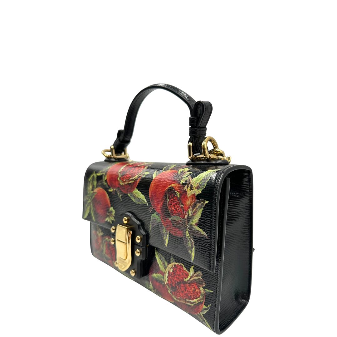 Laterale destro di una borsa D&G in pelle nera con stampa melograni e parti metalliche dorate; munita di un manico rigido fisso e una tracolla in pelle regolabile ed amovibile. Completa di dustbag.