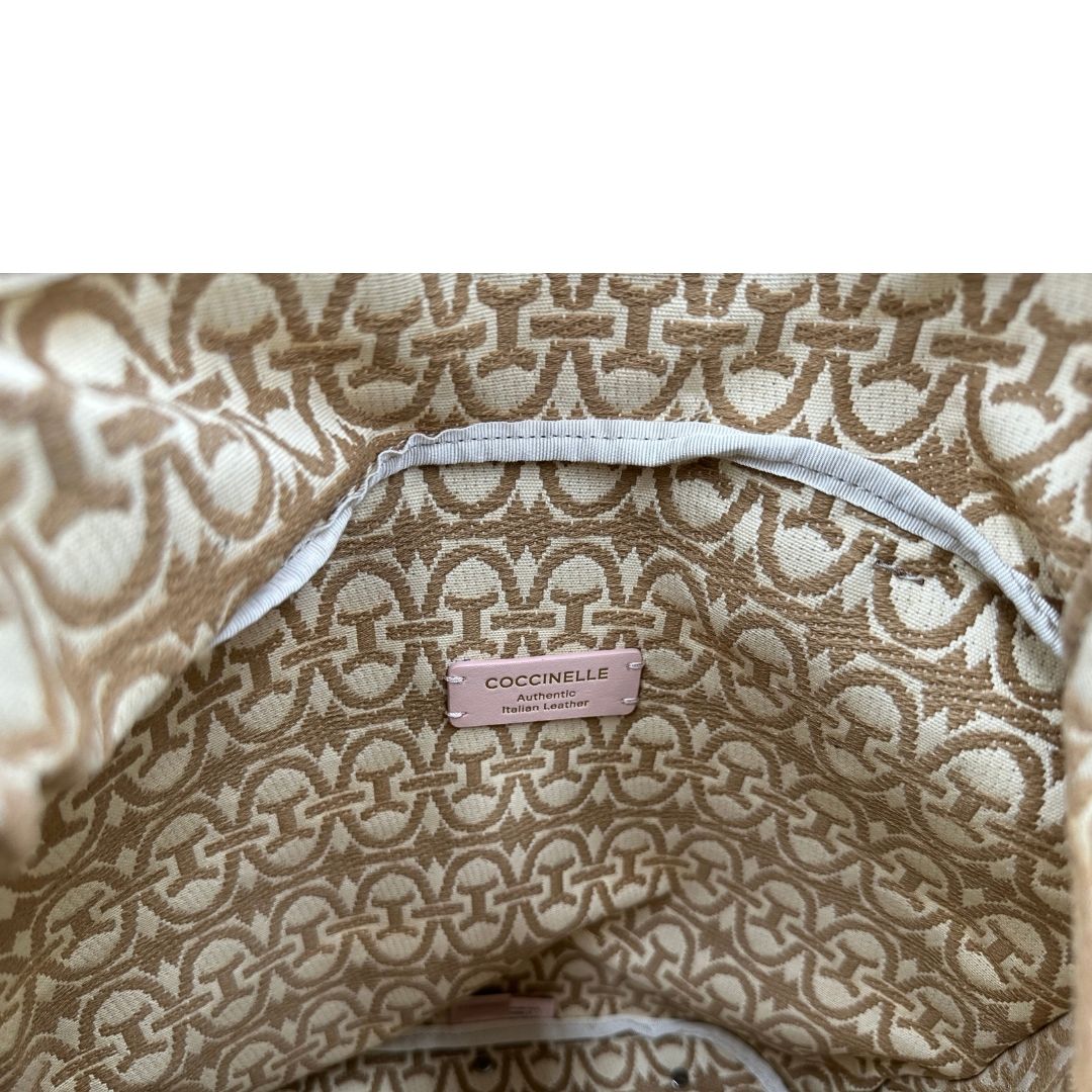 Interno di una borsa Coccinelle in pelle color cammello con parti metalliche argentate e interno in tessuto logato; munita di un manico singolo leggermente regolabile. Indossabile a spalla.