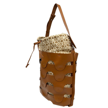 Laterale destro di una borsa Coccinelle in pelle color cammello con parti metalliche argentate e interno in tessuto logato; munita di un manico singolo leggermente regolabile. Indossabile a spalla.