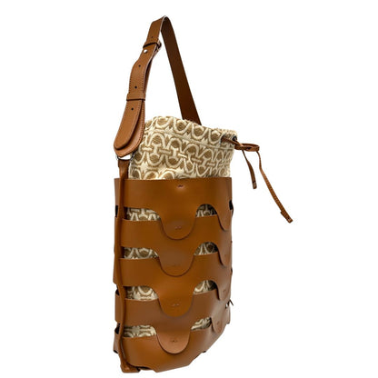 Laterale sinistro di una borsa Coccinelle in pelle color cammello con parti metalliche argentate e interno in tessuto logato; munita di un manico singolo leggermente regolabile. Indossabile a spalla.