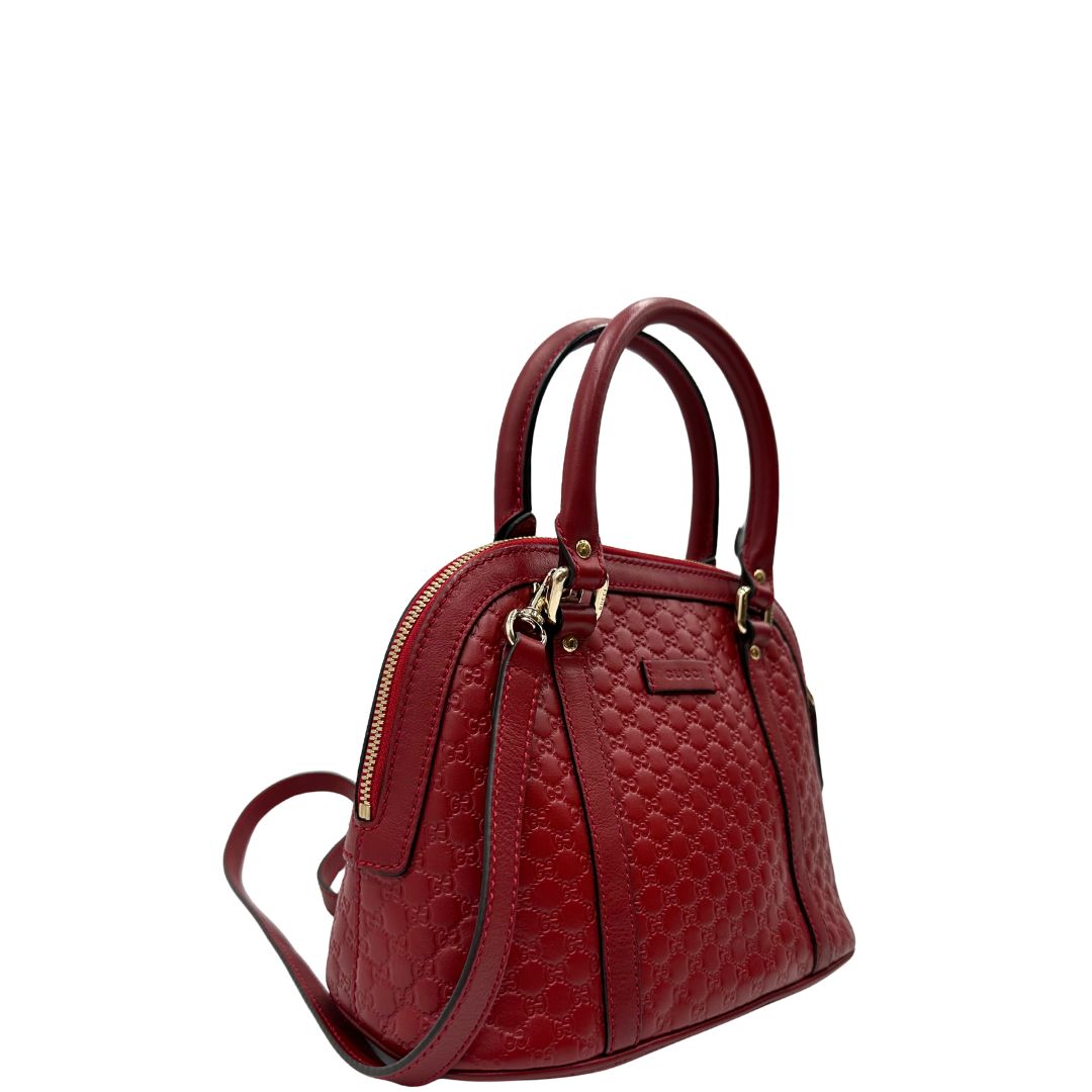 Laterale sinistro di una tracolla Gucci Microguccissima in color rosso ciliegia, con metalleria dorata, usata, originale, second hand, in ottime condizioni.