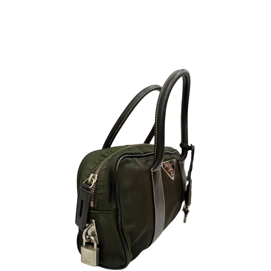 Laterale sinistro di un bauletto Prada in tessuto nylon verde militare e pelle marrone, con dettagli metallici argentati, indossabile a mano.