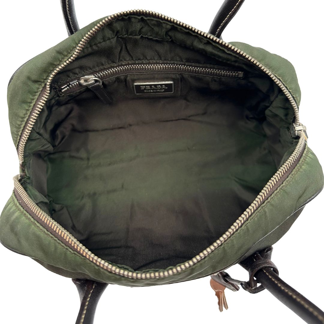 Interno di un bauletto Prada in tessuto nylon verde militare e pelle marrone, con dettagli metallici argentati, indossabile a mano.