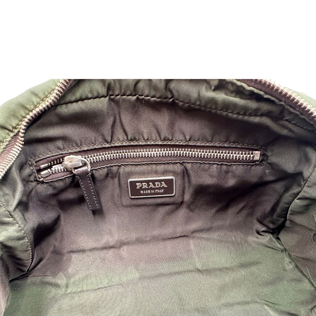 Interno di un bauletto Prada in tessuto nylon verde militare e pelle marrone, con dettagli metallici argentati, indossabile a mano.