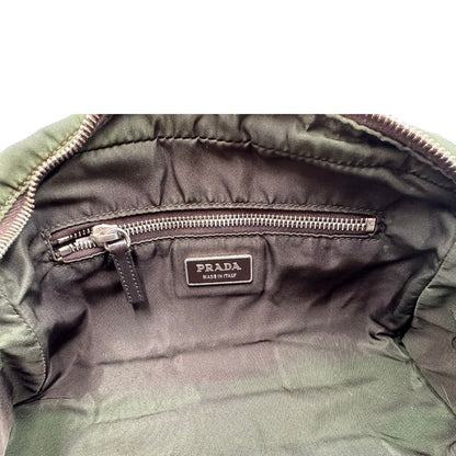 Interno di un bauletto Prada in tessuto nylon verde militare e pelle marrone, con dettagli metallici argentati, indossabile a mano.