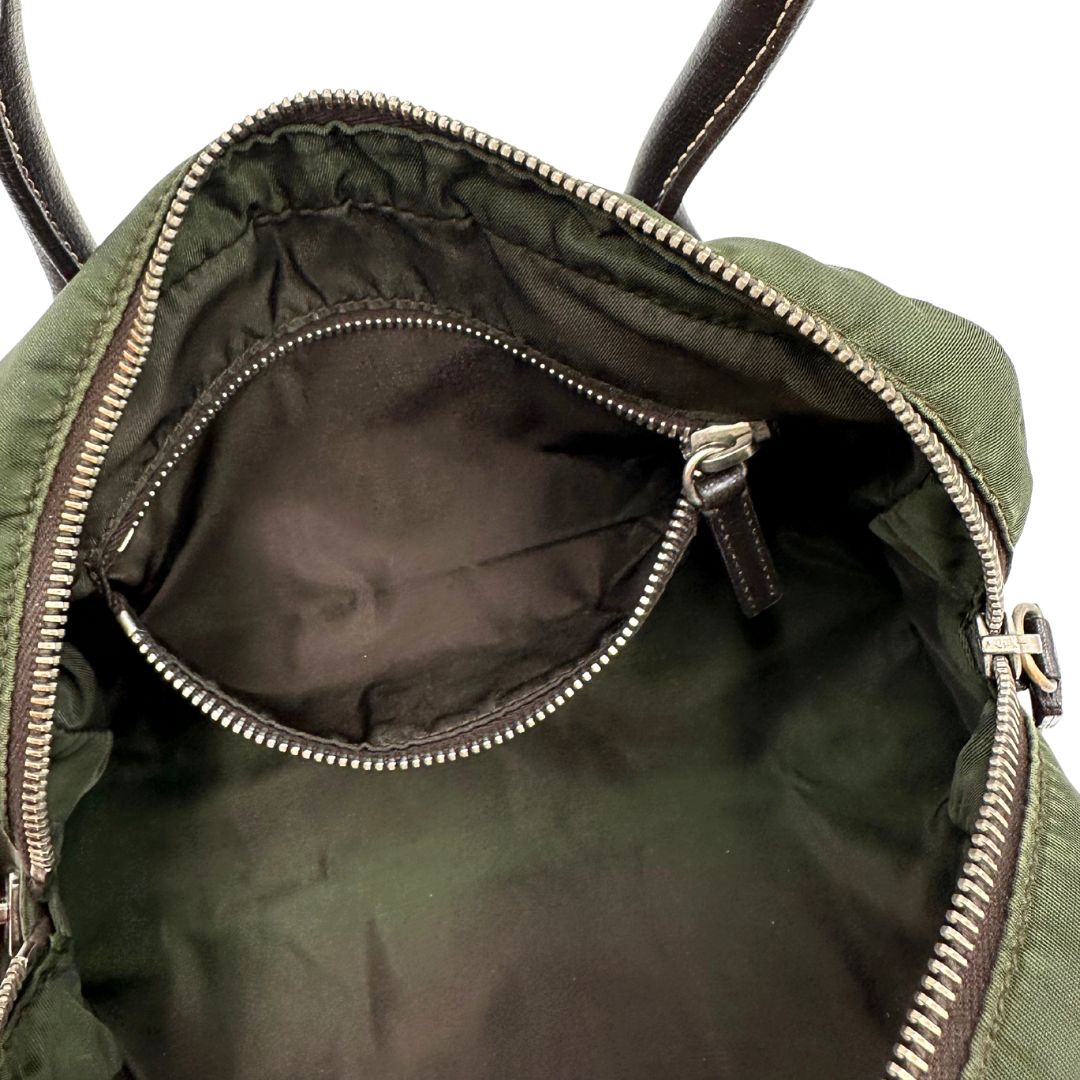 Interno di un bauletto Prada in tessuto nylon verde militare e pelle marrone, con dettagli metallici argentati, indossabile a mano.