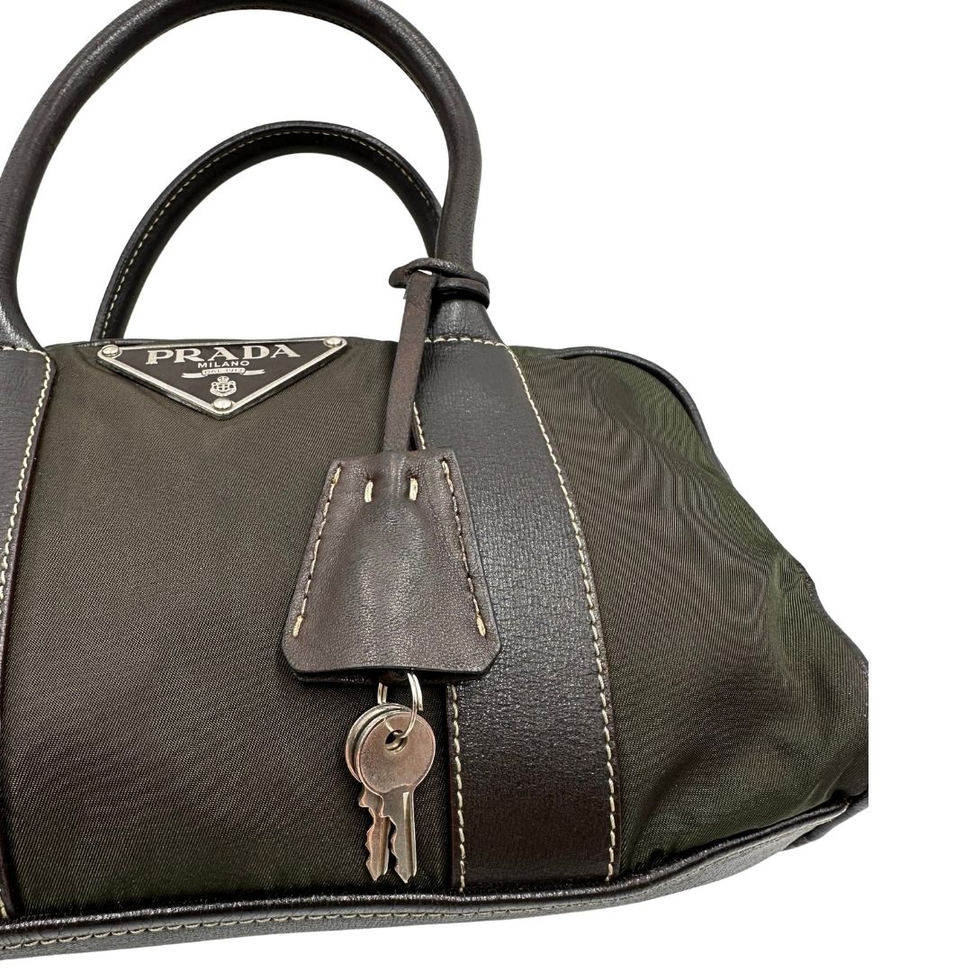 Clochette portachiavi di un bauletto Prada in tessuto nylon verde militare e pelle marrone, con dettagli metallici argentati, indossabile a mano.