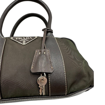 Clochette portachiavi di un bauletto Prada in tessuto nylon verde militare e pelle marrone, con dettagli metallici argentati, indossabile a mano.