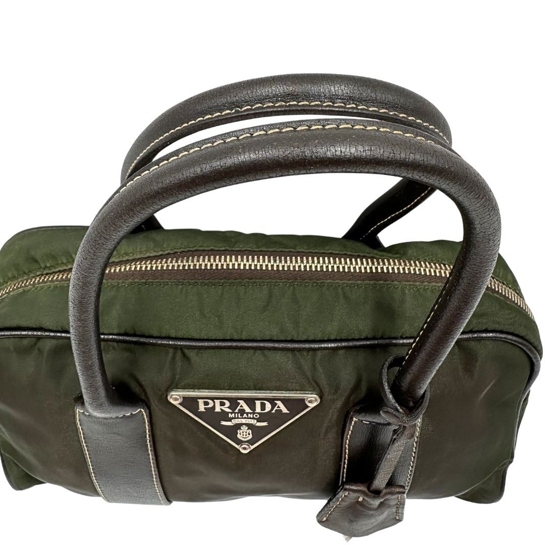 Manici di un bauletto Prada in tessuto nylon verde militare e pelle marrone, con dettagli metallici argentati, indossabile a mano.
