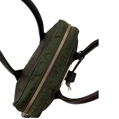 Apertura di un bauletto Prada in tessuto nylon verde militare e pelle marrone, con dettagli metallici argentati, indossabile a mano.