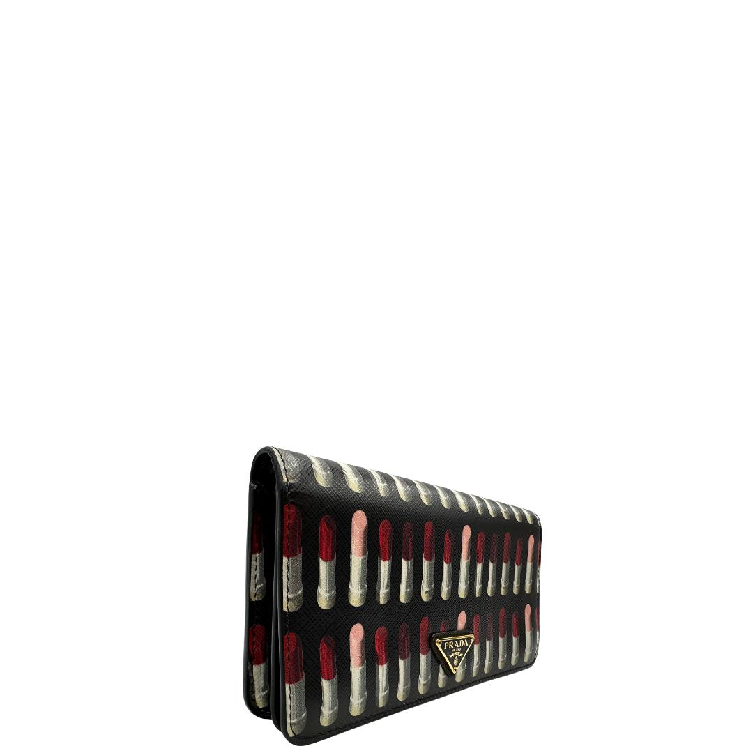 Laterale sinistro di un Prada WOC in pelle saffiano nera, decorato con una vivace stampa di rossetti. Indossabile a tracolla oppure a mano, usato, originale, second hand, in ottime condizioni.