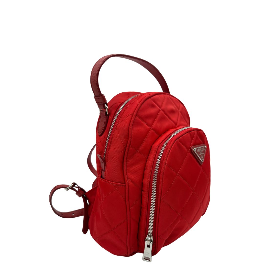 Laterale sinistro di uno zaino Prada in tessuto sintetico rosso e finiture in pelle tono su tono, usato, originale, second hand, in ottime condizioni.