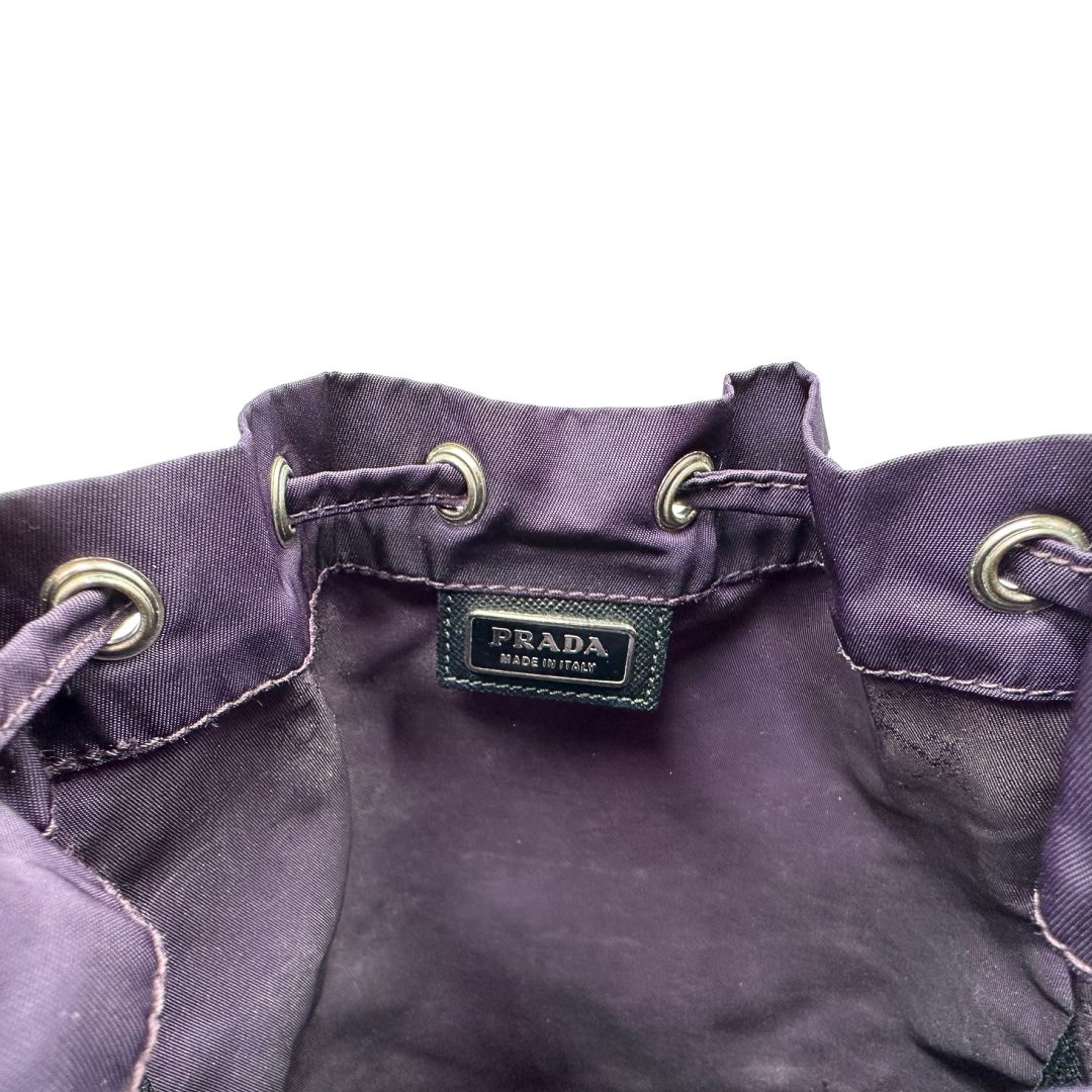 Logo di una pochette Prada in tessuto nylon viola e hardware argentato, usata, originale, second hand, in ottime condizioni.
