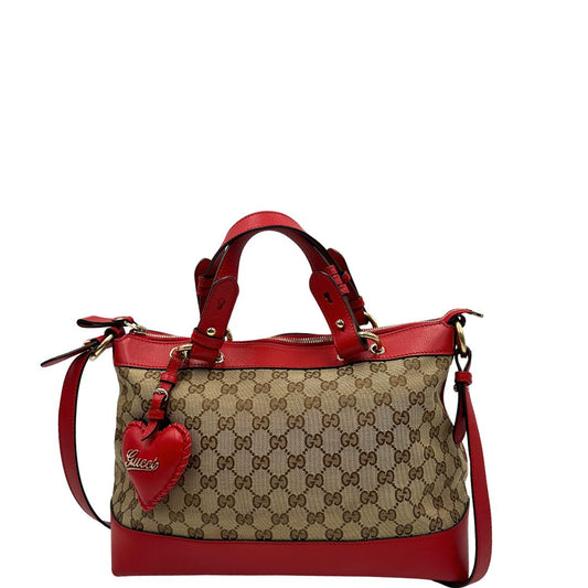 Front di una borsa Gucci in tessuto beige trama GG, con finiture in pelle rosse e romantico charm a forma di cuore, usata, originale, second hand, in ottime condizioni.
