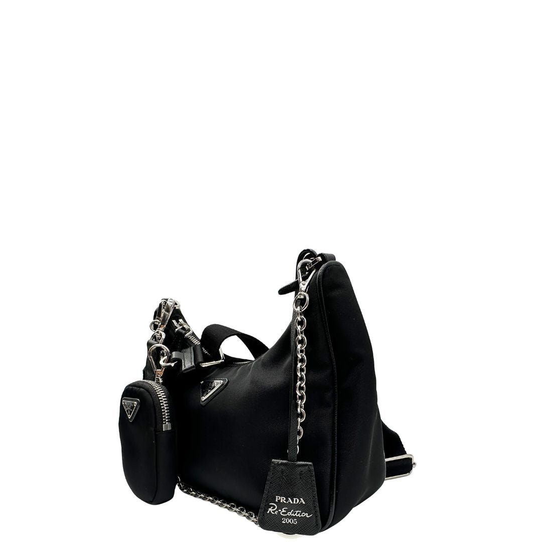 Laterale destro di una borsa Prada Re-Edition 2005 in nylon nero con dettagli in pelle e hardware argento, arricchita da catena frontale, mini pouch removibile e portachiavi logato. Modello compatto e versatile, utilizzabile a spalla, a mano o crossbody, usata, originale, second hand, in condizioni eccellenti.