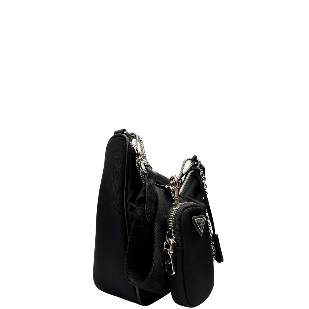 Laterale sinistro di una borsa Prada Re-Edition 2005 in nylon nero con dettagli in pelle e hardware argento, arricchita da catena frontale, mini pouch removibile e portachiavi logato. Modello compatto e versatile, utilizzabile a spalla, a mano o crossbody, usata, originale, second hand, in condizioni eccellenti.
