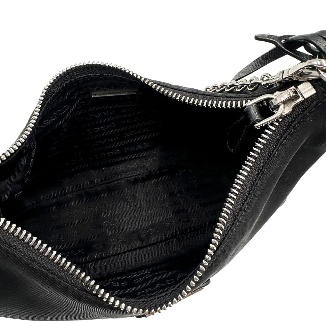 Interno di una borsa Prada Re-Edition 2005 in nylon nero con dettagli in pelle e hardware argento, arricchita da catena frontale, mini pouch removibile e portachiavi logato. Modello compatto e versatile, utilizzabile a spalla, a mano o crossbody, usata, originale, second hand, in condizioni eccellenti.