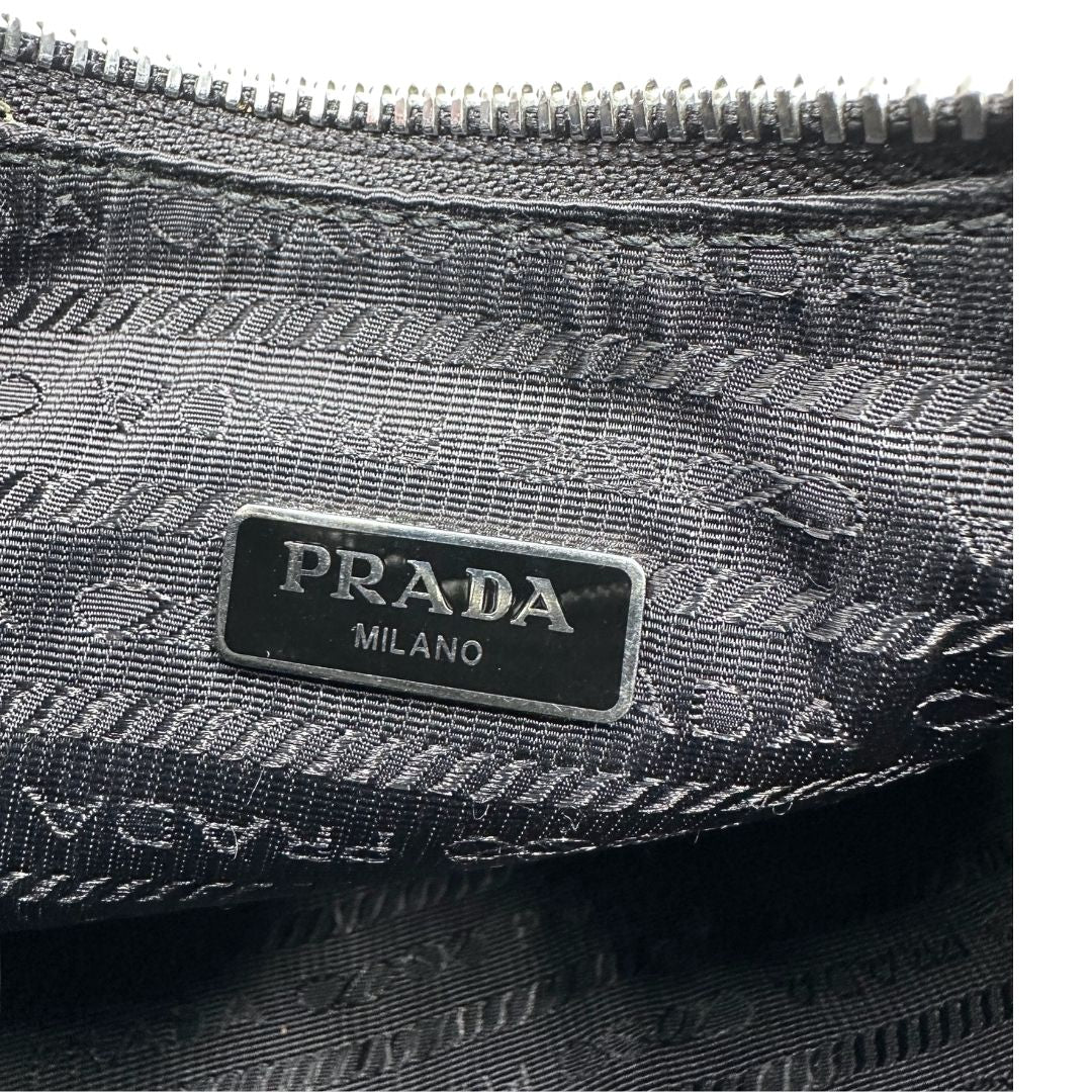 Logo interno di una borsa Prada Re-Edition 2005 in nylon nero con dettagli in pelle e hardware argento, arricchita da catena frontale, mini pouch removibile e portachiavi logato. Modello compatto e versatile, utilizzabile a spalla, a mano o crossbody, usata, originale, second hand, in condizioni eccellenti.