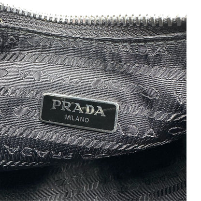 Logo interno di una borsa Prada Re-Edition 2005 in nylon nero con dettagli in pelle e hardware argento, arricchita da catena frontale, mini pouch removibile e portachiavi logato. Modello compatto e versatile, utilizzabile a spalla, a mano o crossbody, usata, originale, second hand, in condizioni eccellenti.