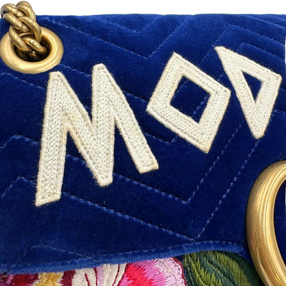 Ingiallimento sulla scritta decorativa di una borsa Gucci Marmont nella misura grande velvet color blu reale, con patchwork decorativi, usata, originale, second hand, in ottime condizioni.