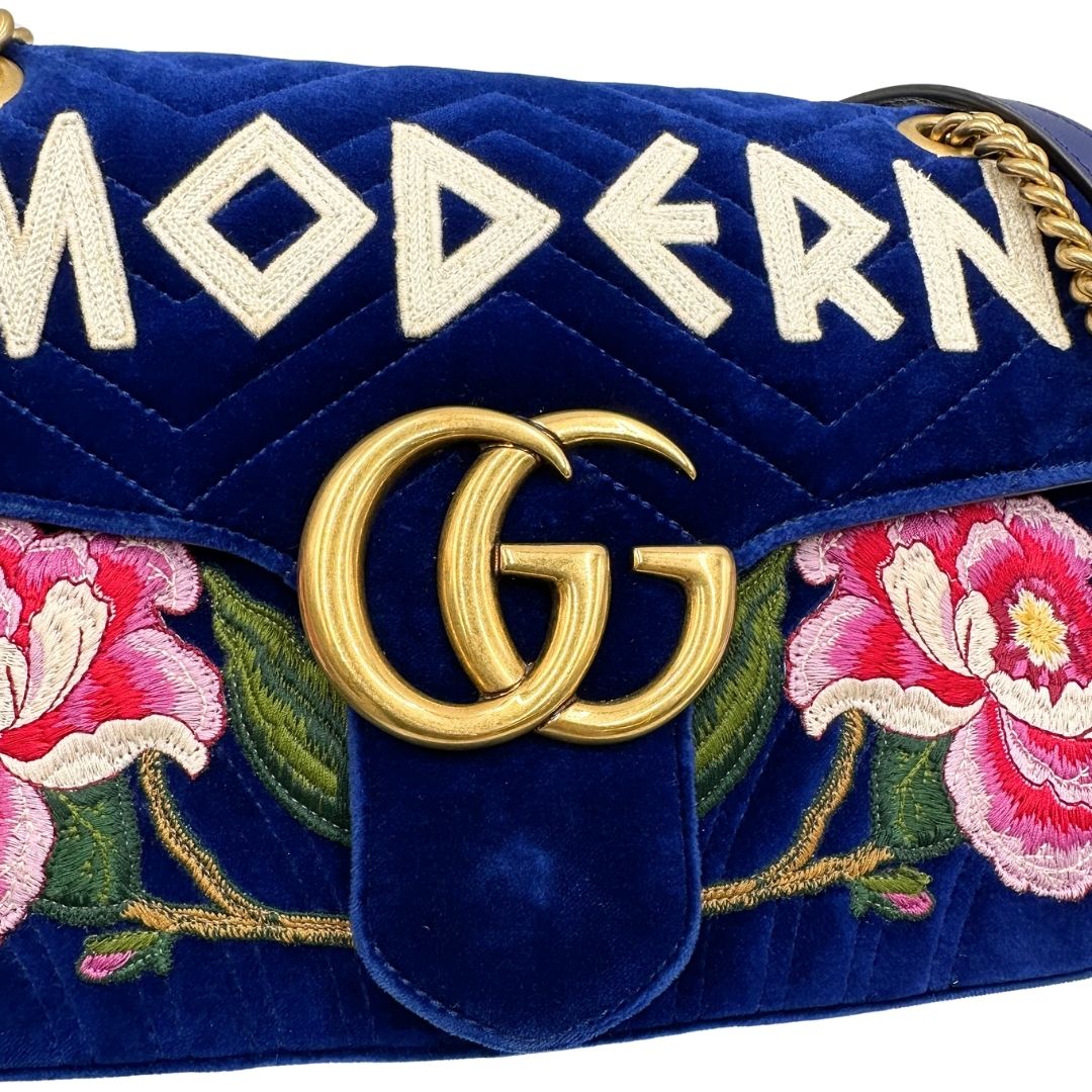 Logo metallico di una borsa Gucci Marmont nella misura grande velvet color blu reale, con patchwork decorativi, usata, originale, second hand, in ottime condizioni.
