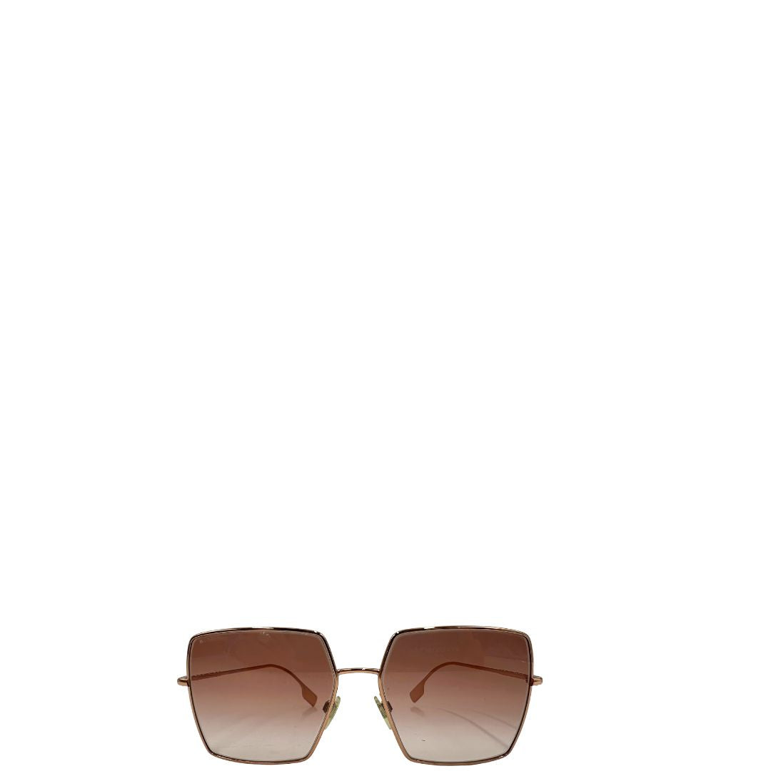 Occhiali da sole Burberry in metallo dorato con una montatura squadrata oversize in metallo, lenti sfumate marroni o rosa.
