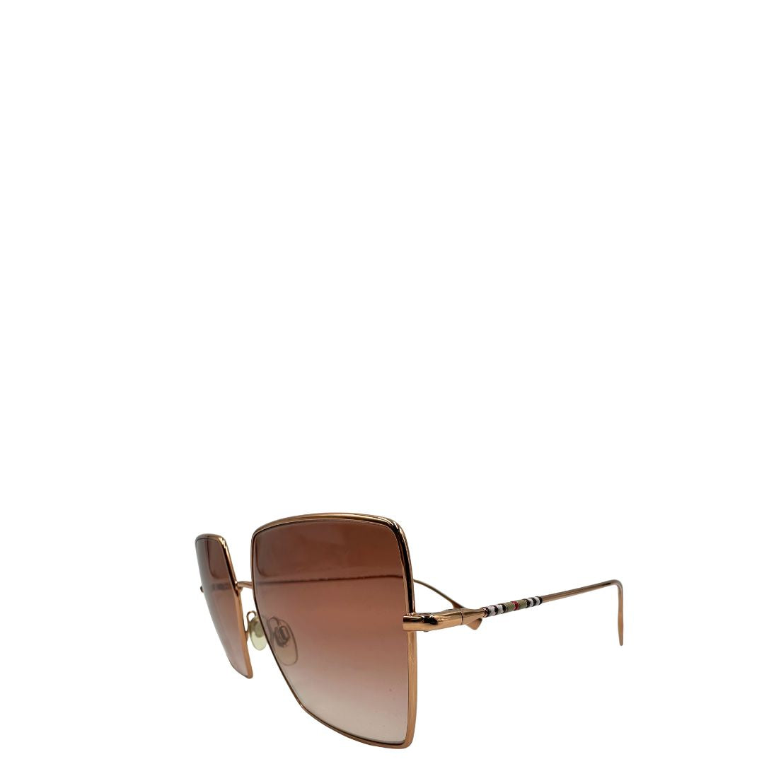 Occhiali da sole Burberry in metallo dorato con una montatura squadrata oversize in metallo, lenti sfumate marroni o rosa.