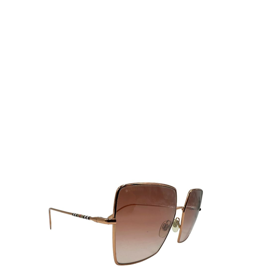 Occhiali da sole Burberry in metallo dorato con una montatura squadrata oversize in metallo, lenti sfumate marroni o rosa.