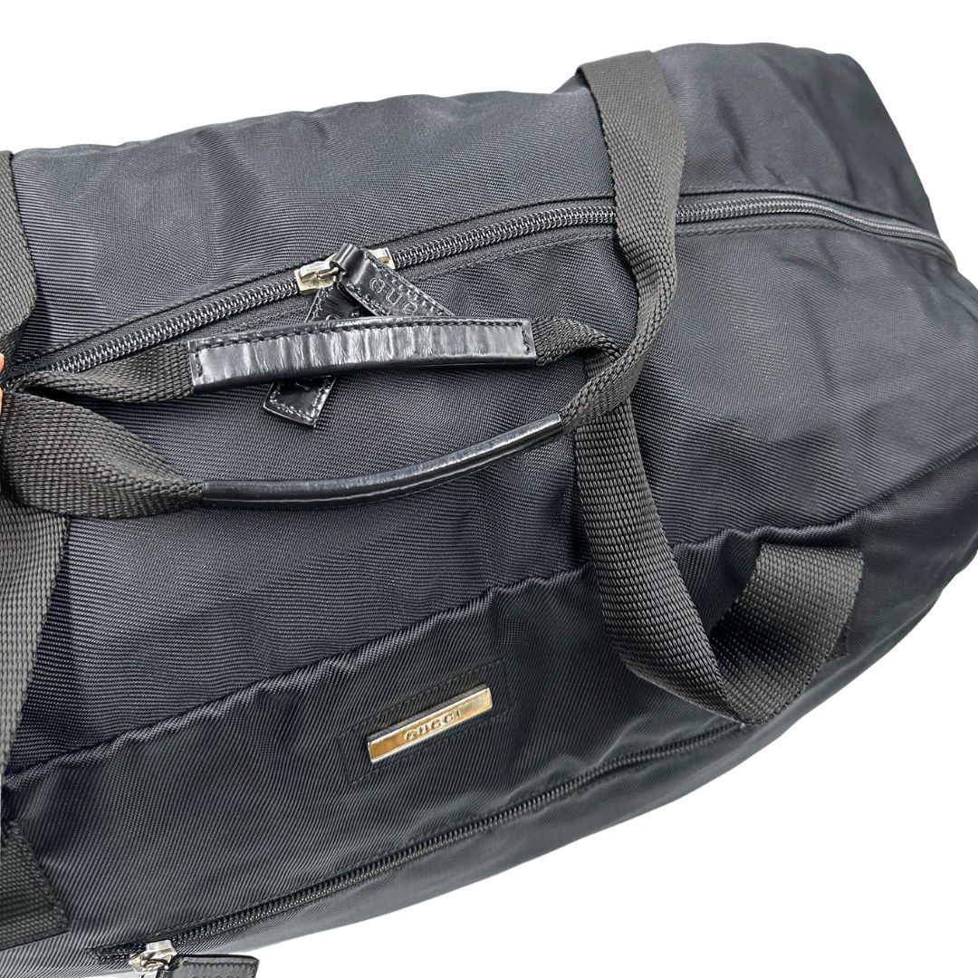 Manici di un borsone Gucci in tela nera, con dettagli in pelle tono su tono, usato, originale, second hand, in ottime condizioni.