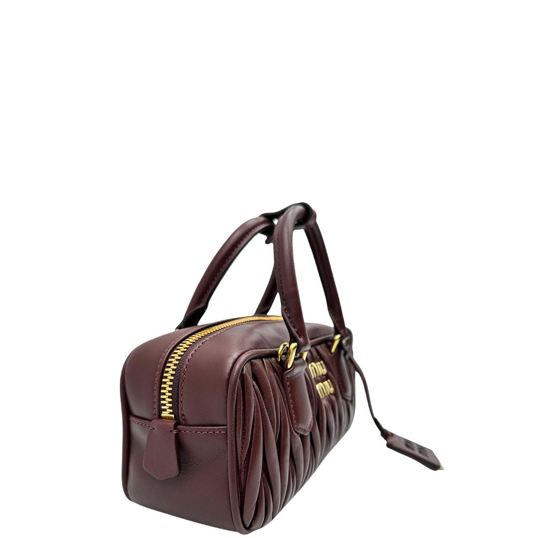 Lato, Borsa Miu Miu Arcadie realizzata in nappa matelassé bordeaux con la classica silhouette del bauletto. Da portare a mano o a tracolla. Originale, usata, di lusso, in condizioni eccellenti.