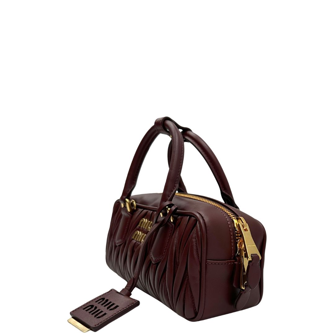 Lato, Borsa Miu Miu Arcadie realizzata in nappa matelassé bordeaux con la classica silhouette del bauletto. Da portare a mano o a tracolla. Originale, usata, di lusso, in condizioni eccellenti.