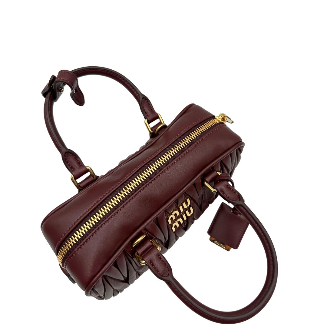 Chiusura, Borsa Miu Miu Arcadie realizzata in nappa matelassé bordeaux con la classica silhouette del bauletto. Da portare a mano o a tracolla. Originale, usata, di lusso, in condizioni eccellenti.