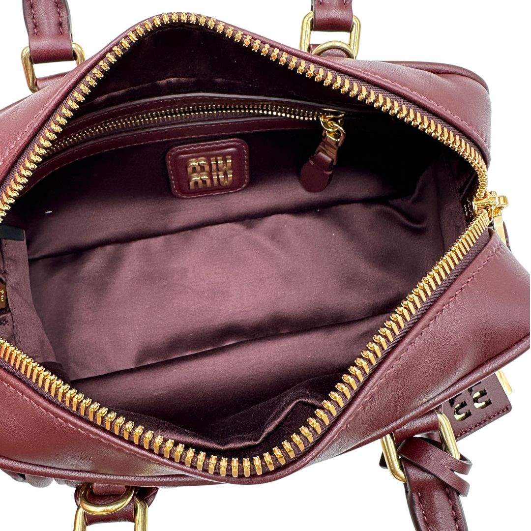 Interno, Borsa Miu Miu Arcadie realizzata in nappa matelassé bordeaux con la classica silhouette del bauletto. Da portare a mano o a tracolla. Originale, usata, di lusso, in condizioni eccellenti.
