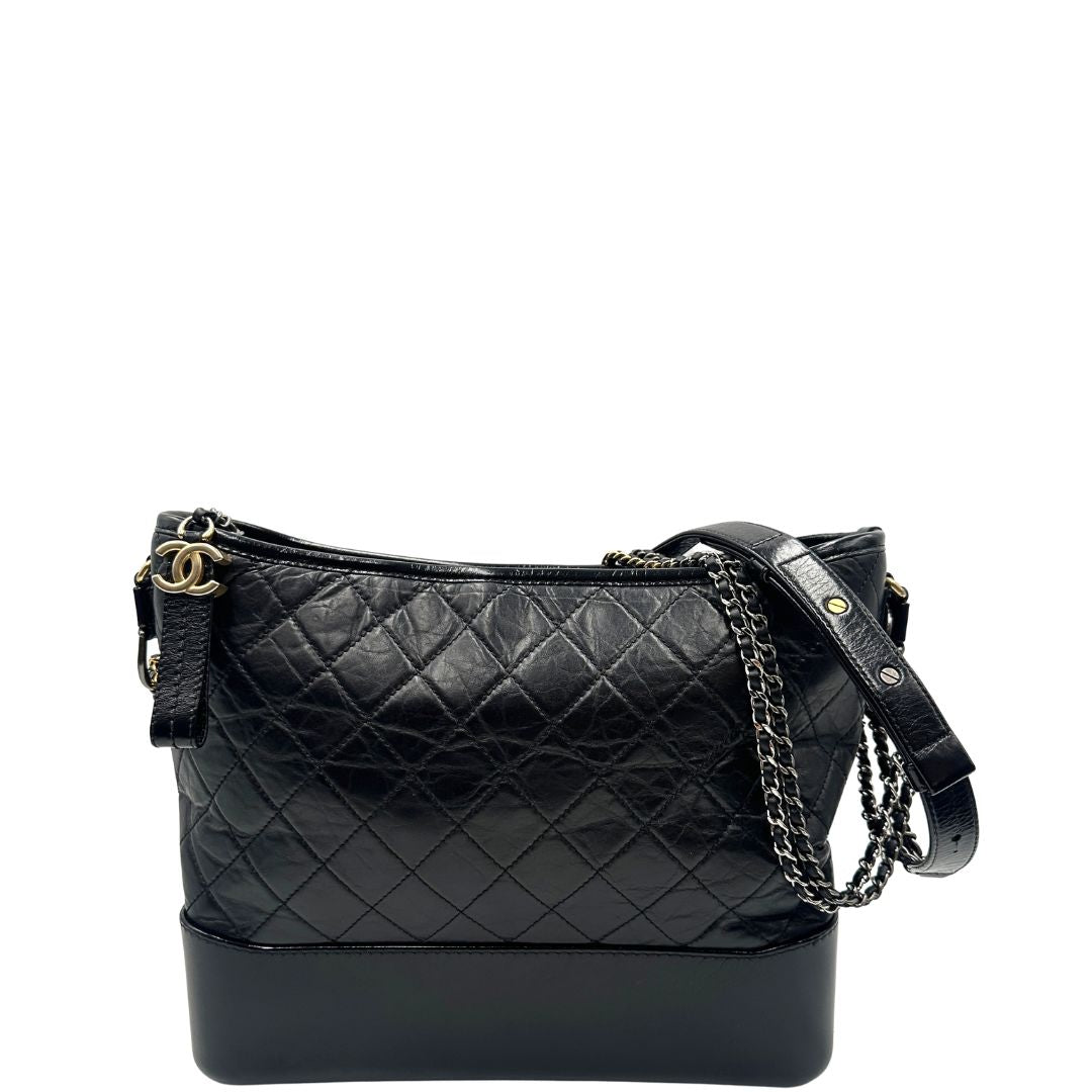 front Chanel Gabrielle Hobo Bag in pelle di vitello trapuntata nera, caratterizzata da una solida base rigida inferiore, dettagli con finiture miste color oro e argento e una tracolla regolabile a catena intrecciata in pelle 