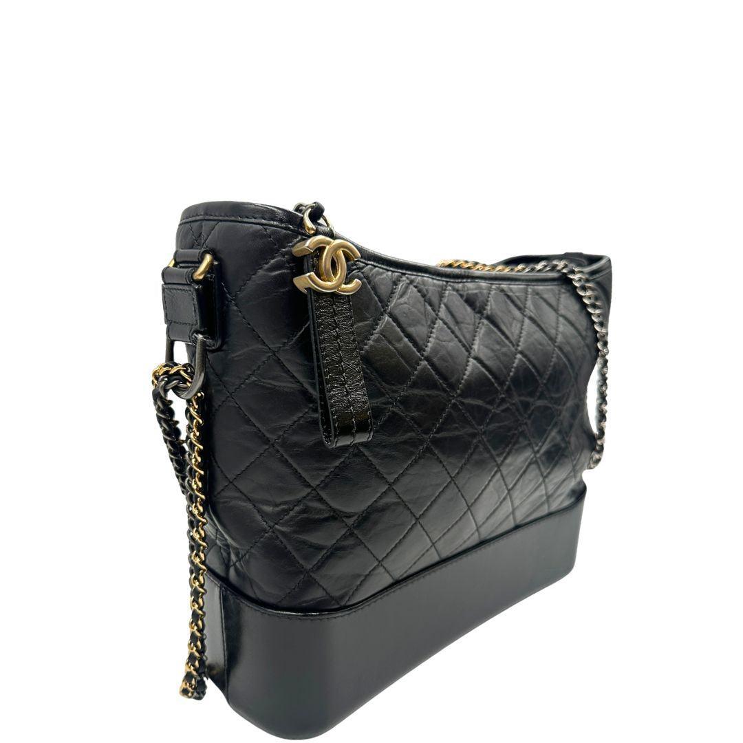 lato Chanel Gabrielle Hobo Bag in pelle di vitello trapuntata nera, caratterizzata da una solida base rigida inferiore, dettagli con finiture miste color oro e argento e una tracolla regolabile a catena intrecciata in pelle 