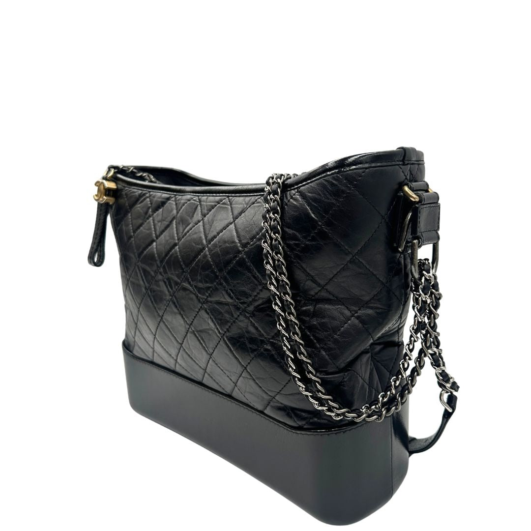 lato Chanel Gabrielle Hobo Bag in pelle di vitello trapuntata nera, caratterizzata da una solida base rigida inferiore, dettagli con finiture miste color oro e argento e una tracolla regolabile a catena intrecciata in pelle 