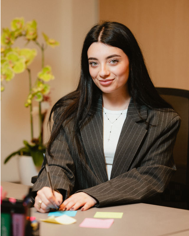 Giovane donna seduta alla scrivania con post-it colorati, capelli lunghi scuri e giacca a righe.
