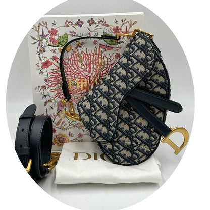 Borsa Saddle Dior in tessuto beige con trama Dior Oblique nera e blu, finiture in pelle blu notte e parti metalliche dorate. Munita di manico singolo e tracolla regolabile, e amovibile. Completa di corredo. Originale, usato, condizioni ottime. 